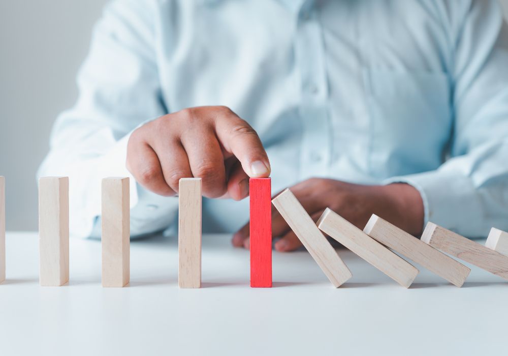 Business man stopping Jenga block from toppling